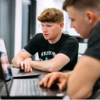 Two students working on their computers together.