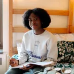 A student sitting on their bed in their dorm.